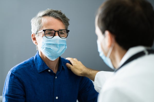 Male patient wearing a mask is comforted by doctor.