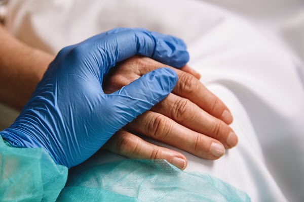 Caregiver hand holds the hand of a patient.