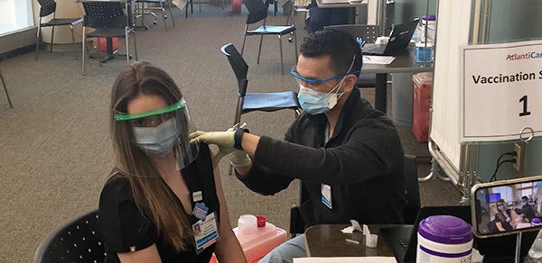 Fourth year medical student Kenneth Lam administers his 100th COVID vaccination to fellow medical student Rachel Fulton.