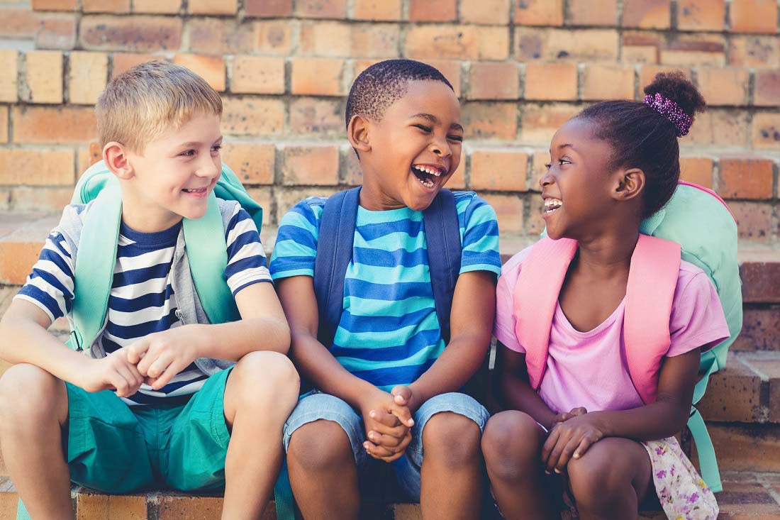 Three children with backpacks sit and wait for first day of school