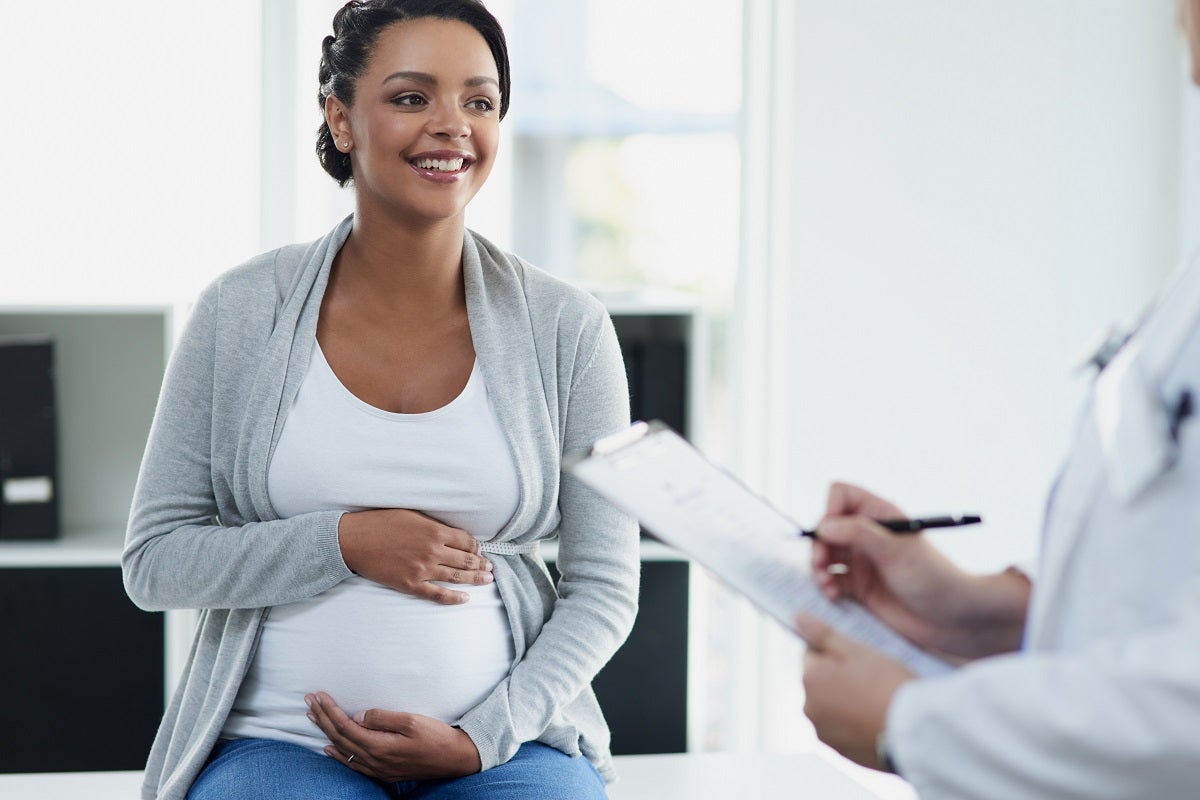 Smiling pregnant woman meets with a provider, her hands placed along her belly.